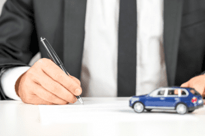 MD bankruptcy attorney completing paperwork next to a blue toy car. Many people believe that an auto loan is a nondischargeable debt, but this is not always the case.